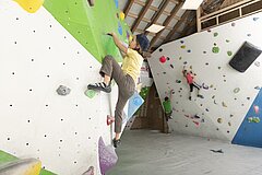 A climbing room with several climbing walls. Two people are actively bouldering.